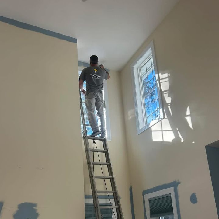 Roll With It painter working on a tall interior wall